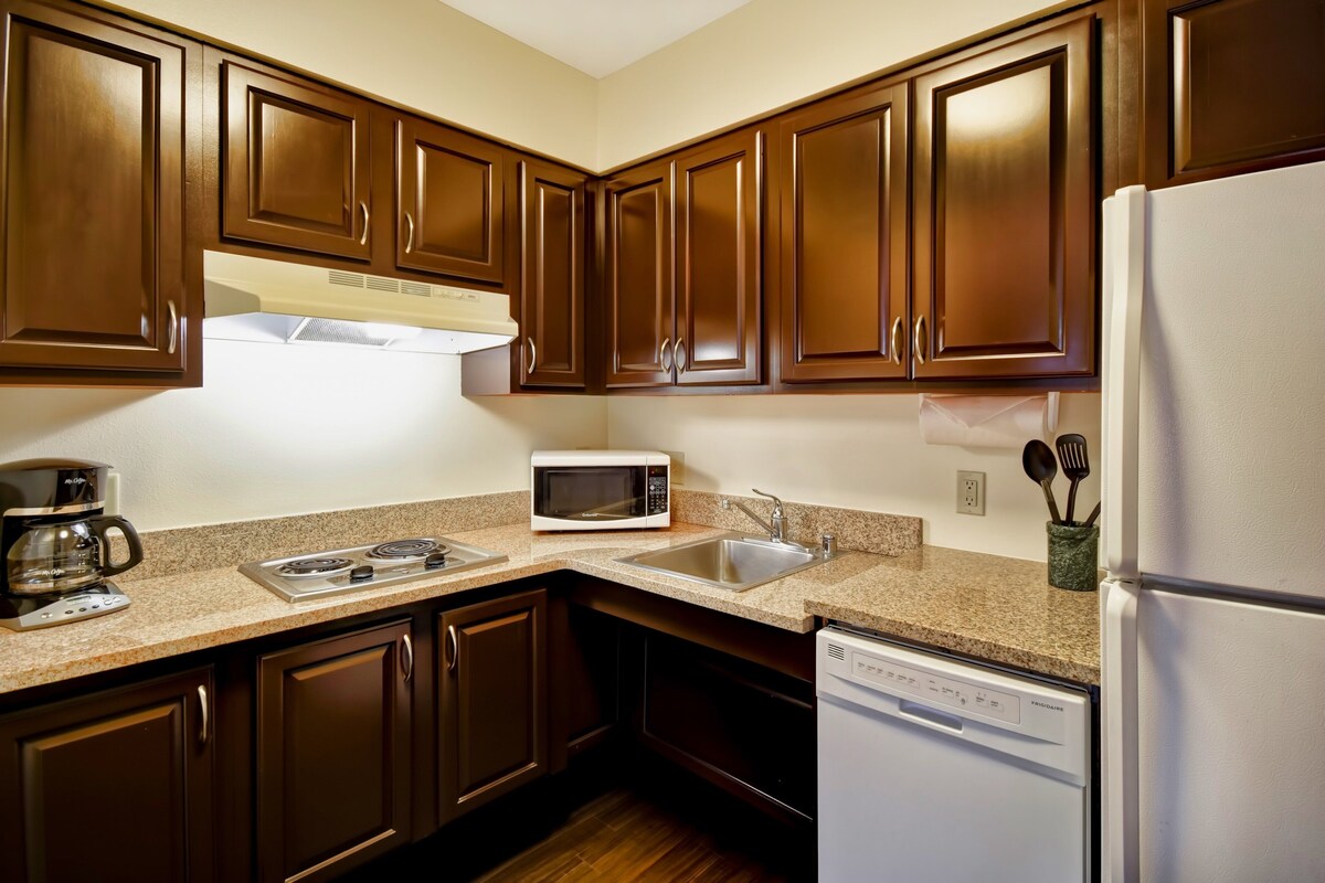 A kitchen with dark wooden cabinets, a white refrigerator, a microwave, a coffee maker, and a dishwasher.