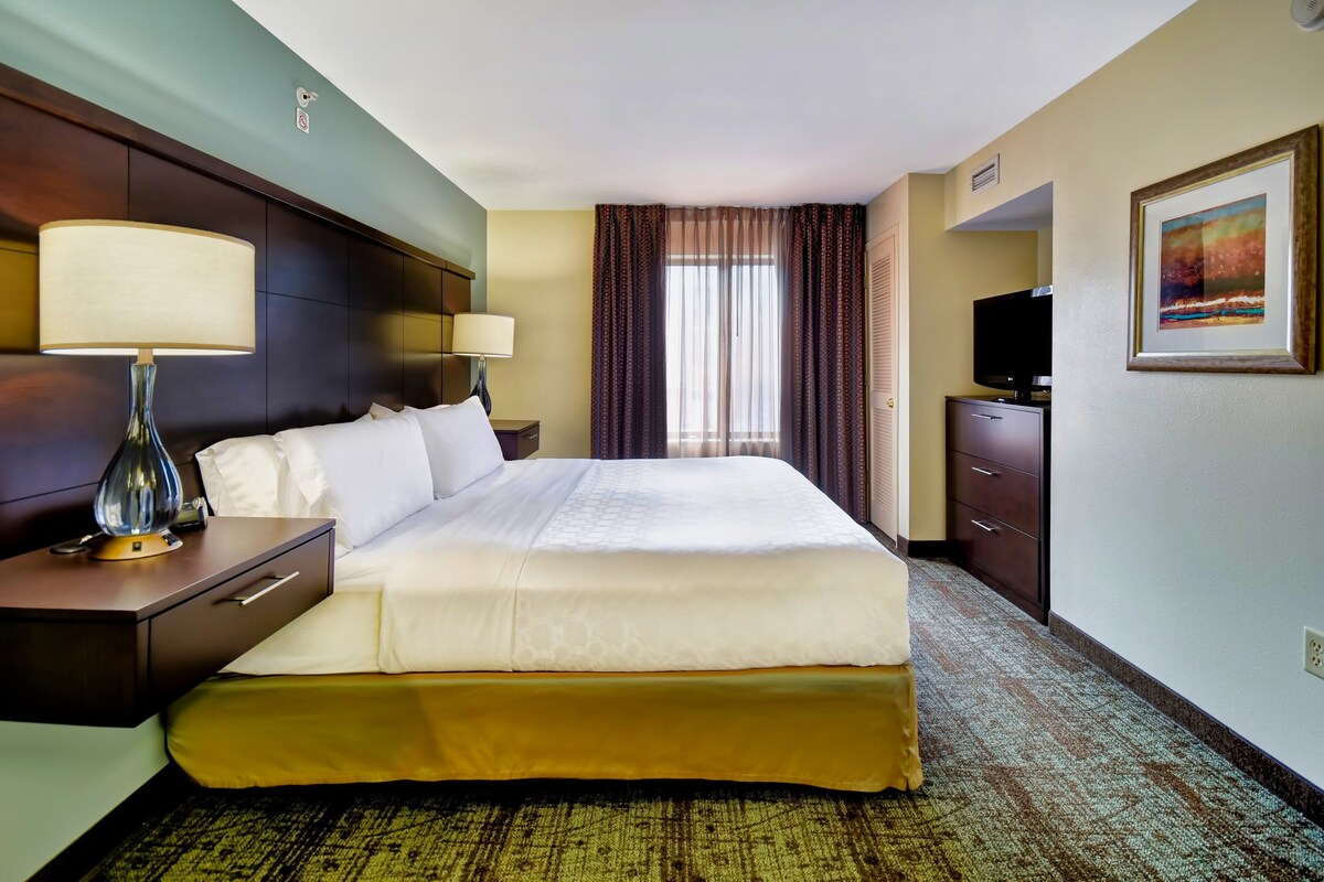 A hotel room with a large bed, two bedside tables with lamps, a dresser, a television, and a framed picture on the wall.