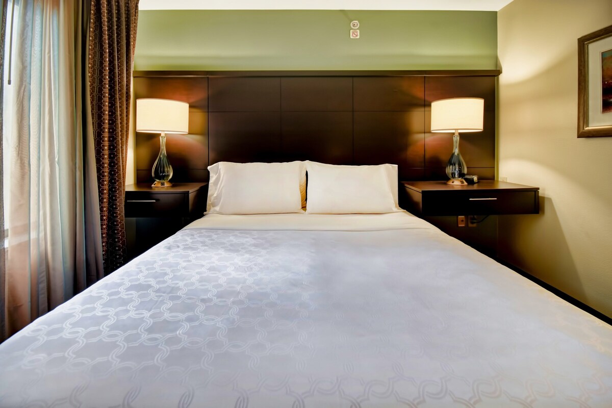 A hotel room with a large bed, two bedside tables with lamps, a headboard, and a framed picture on the wall.