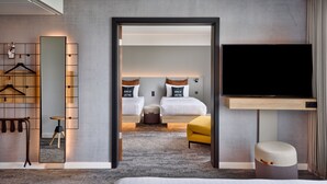 A modern hotel room with a large bed, a TV, a mirror, and a seating area with a small table and chairs.