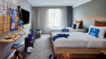 Une chambre d’hôtel comprenant un lit, un bureau, une chaise, une télévision, une fenêtre avec des rideaux et une décoration sur le thème du sport.