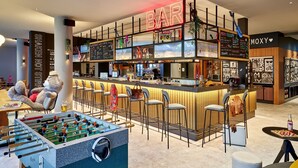 A modern bar area with a foosball table, bar stools, and a neon sign.