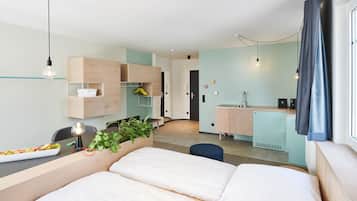 A modern hotel room with a bed, a small desk, a kitchenette, and a bathroom.