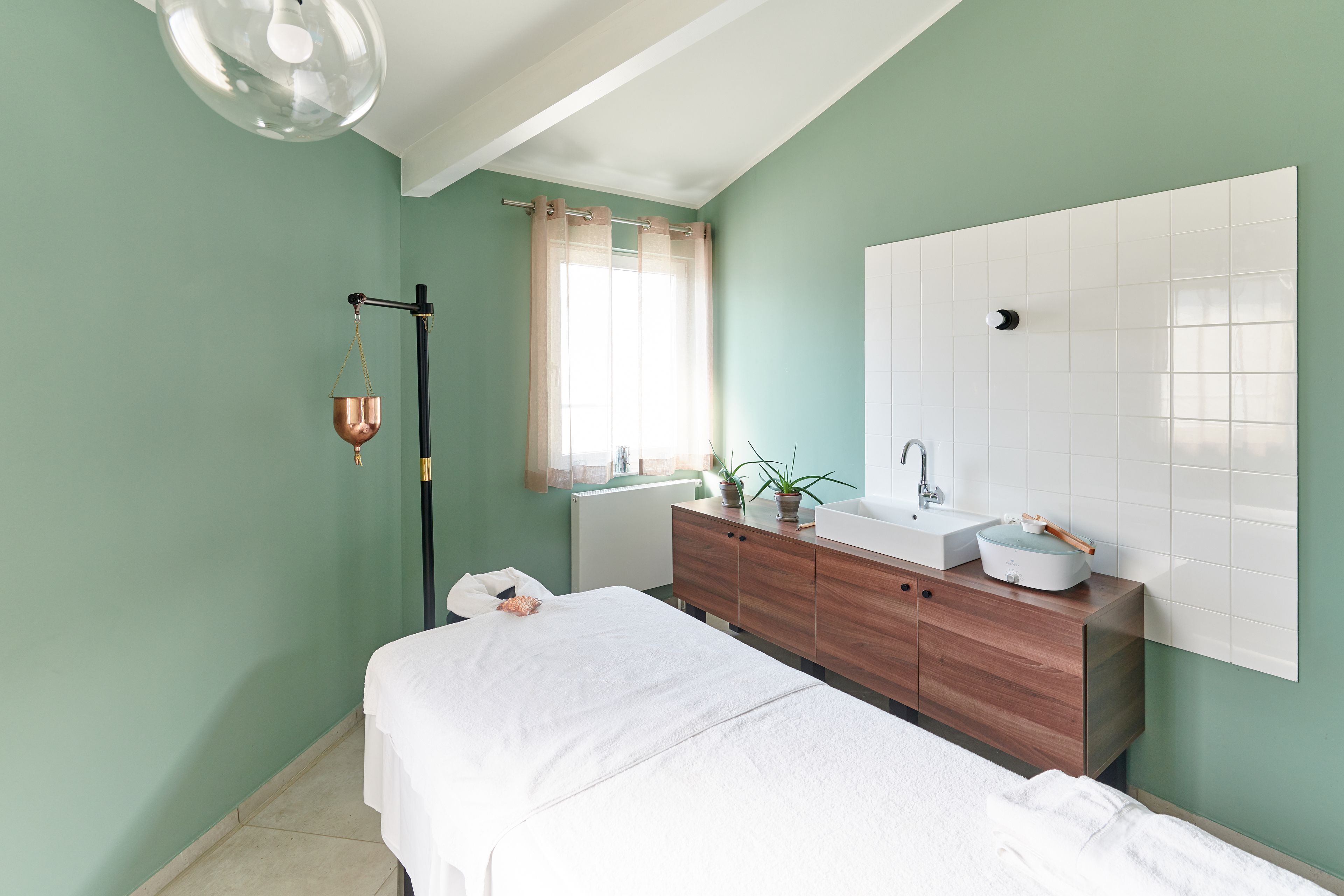 A bedroom with a bed, a wooden dresser, a white sink, and a large mirror.