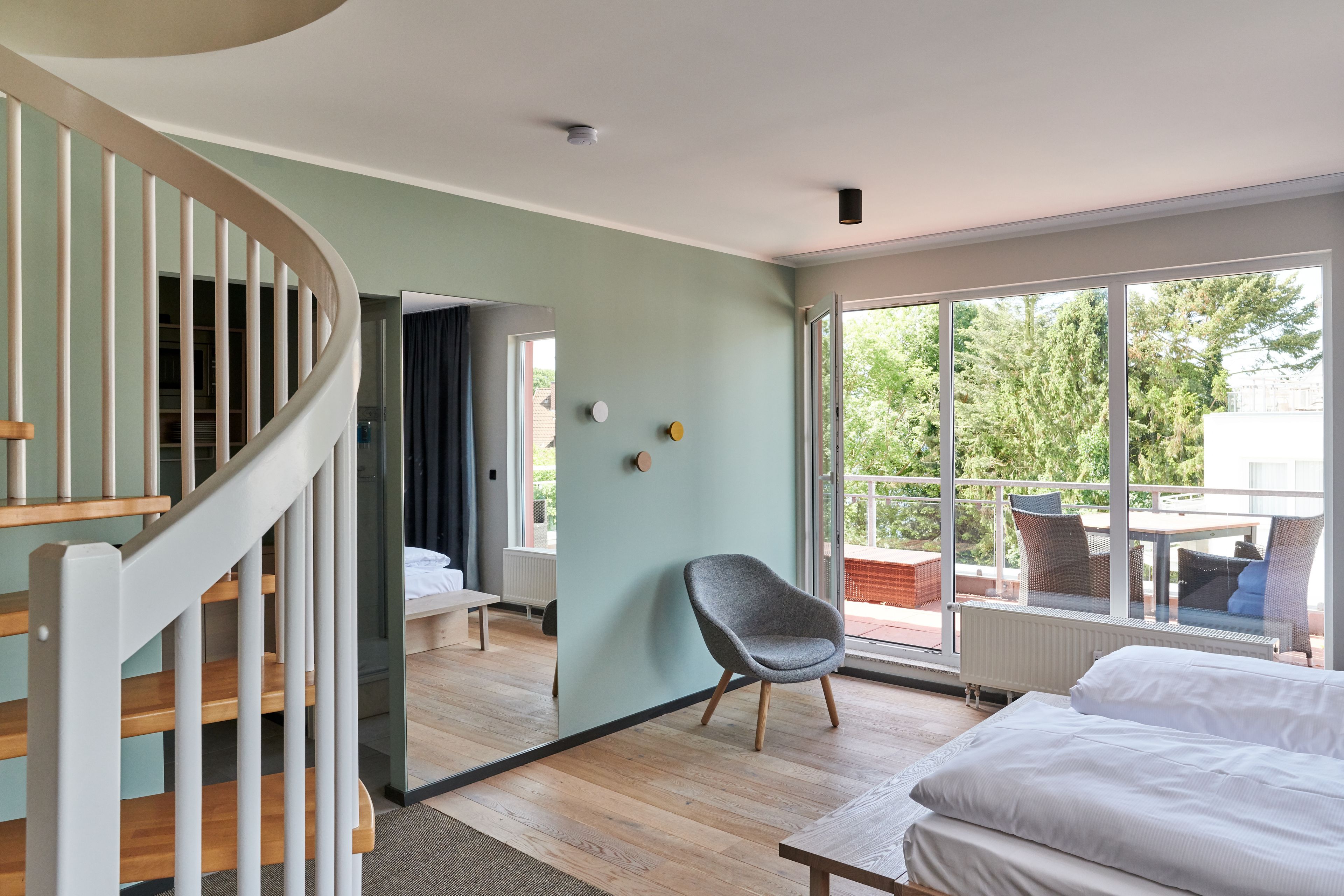 Ein modernes Schlafzimmer mit einer Holztreppe, einem großen Fenster mit Ausblick ins Freie und einer gemütlichen Sitzecke mit Sessel und Tisch.