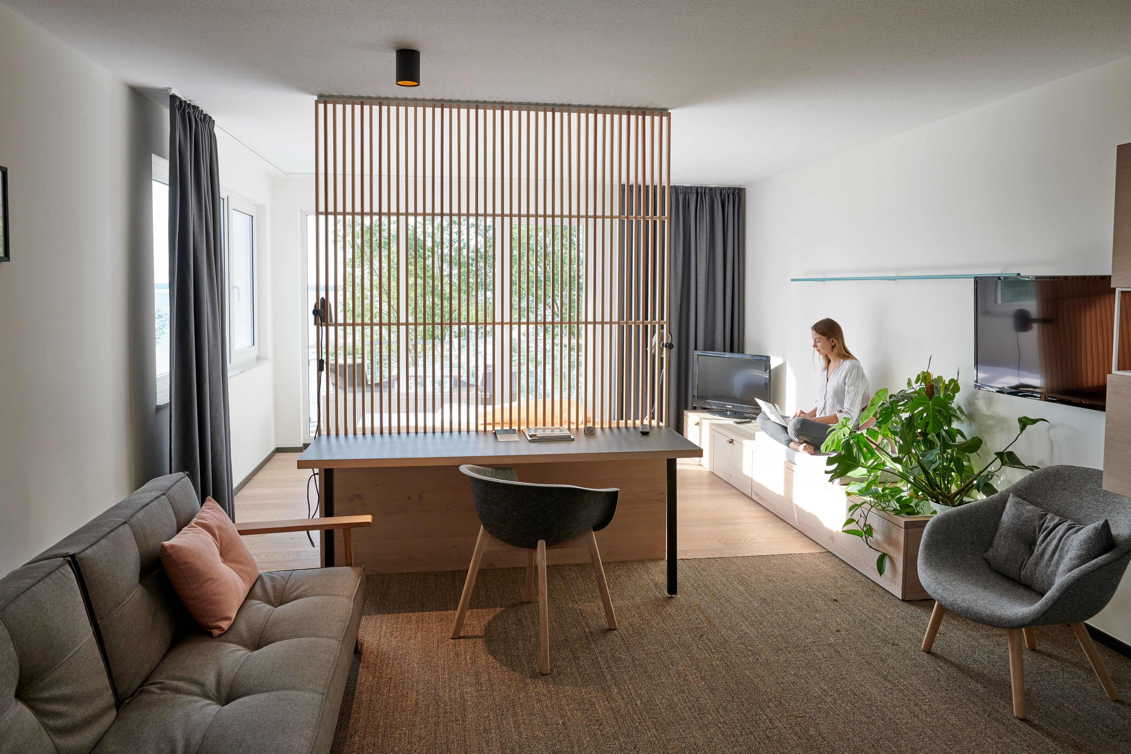 Una sala de estar moderna con un sofá, un escritorio y una silla. Hay un televisor y una planta en el escritorio.