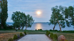 A serene lakeside view with a gravel area, trees, and a bench. - Hotel Whitman (Ascheberg)