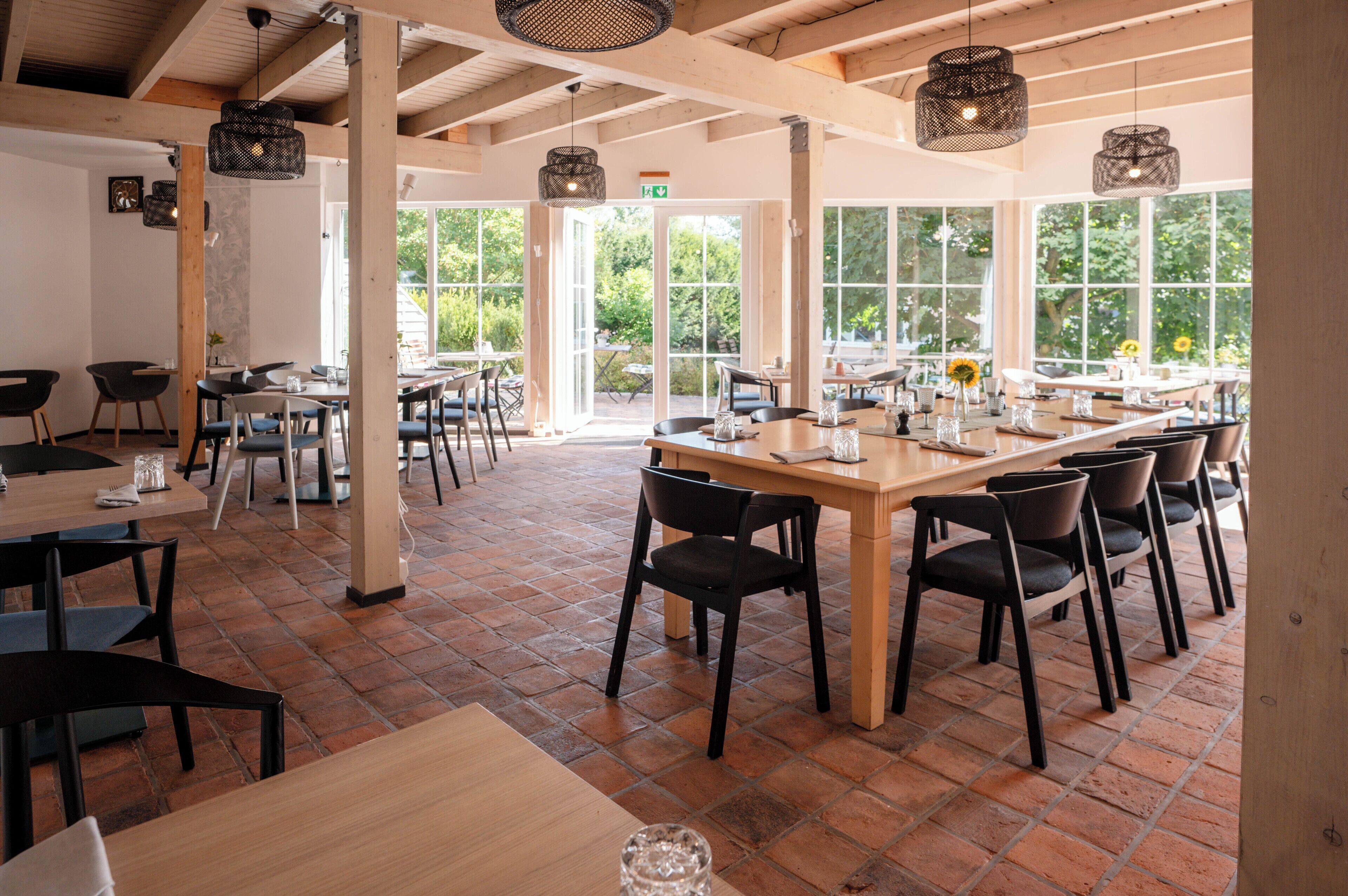 A spacious dining area with large windows, wooden tables, and black chairs.