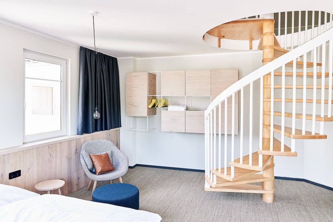 Una habitación de hotel moderna con una escalera de madera, un pequeño rincón de descanso y un armario con espacio para colgar.