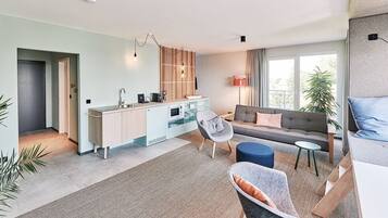 A modern living room with a sofa, armchairs, and a coffee table. There is a kitchen area with a sink and a dining table.