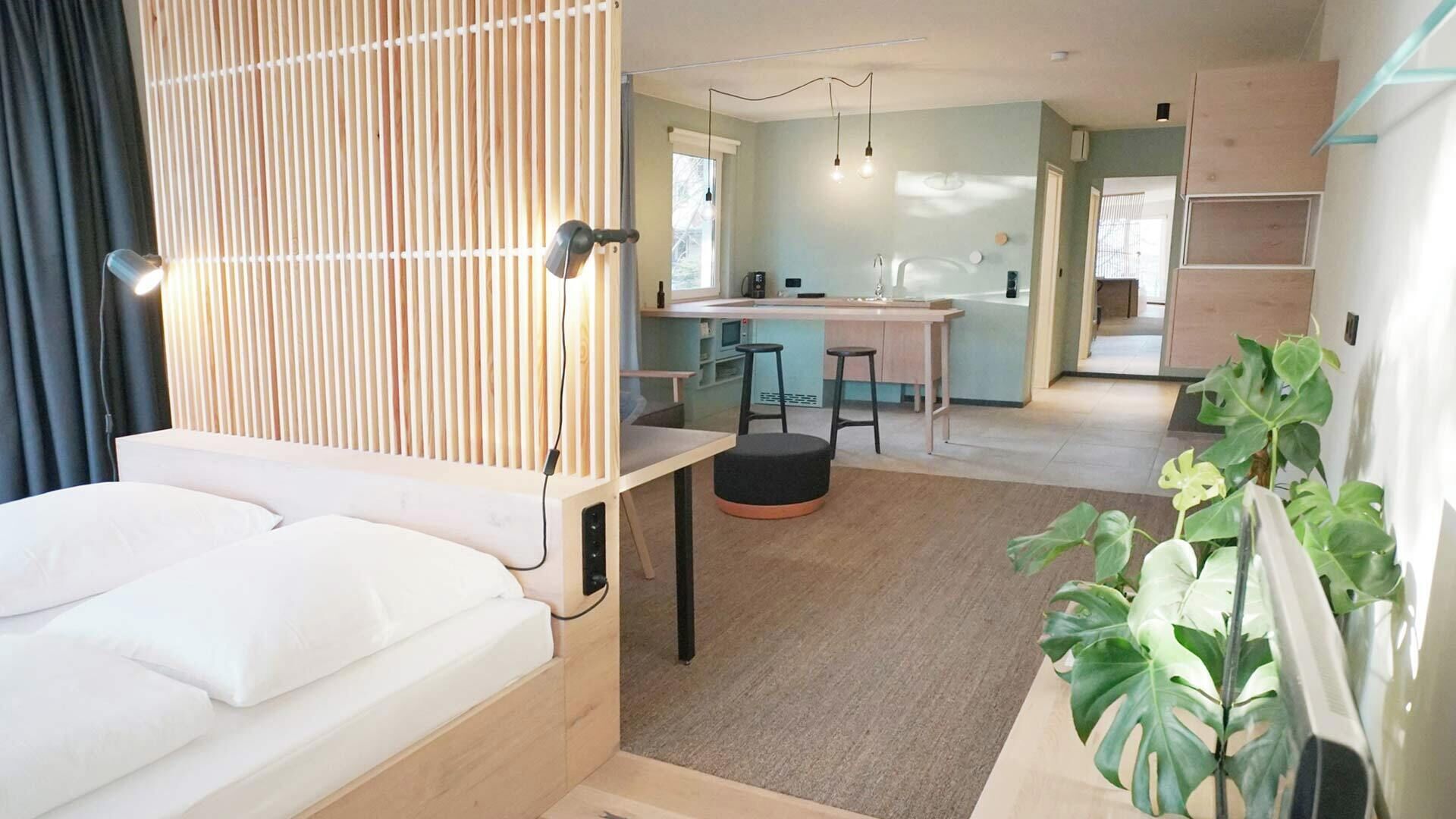 Habitación de hotel moderna con cama, escritorio, kitchenette y zona de comedor.