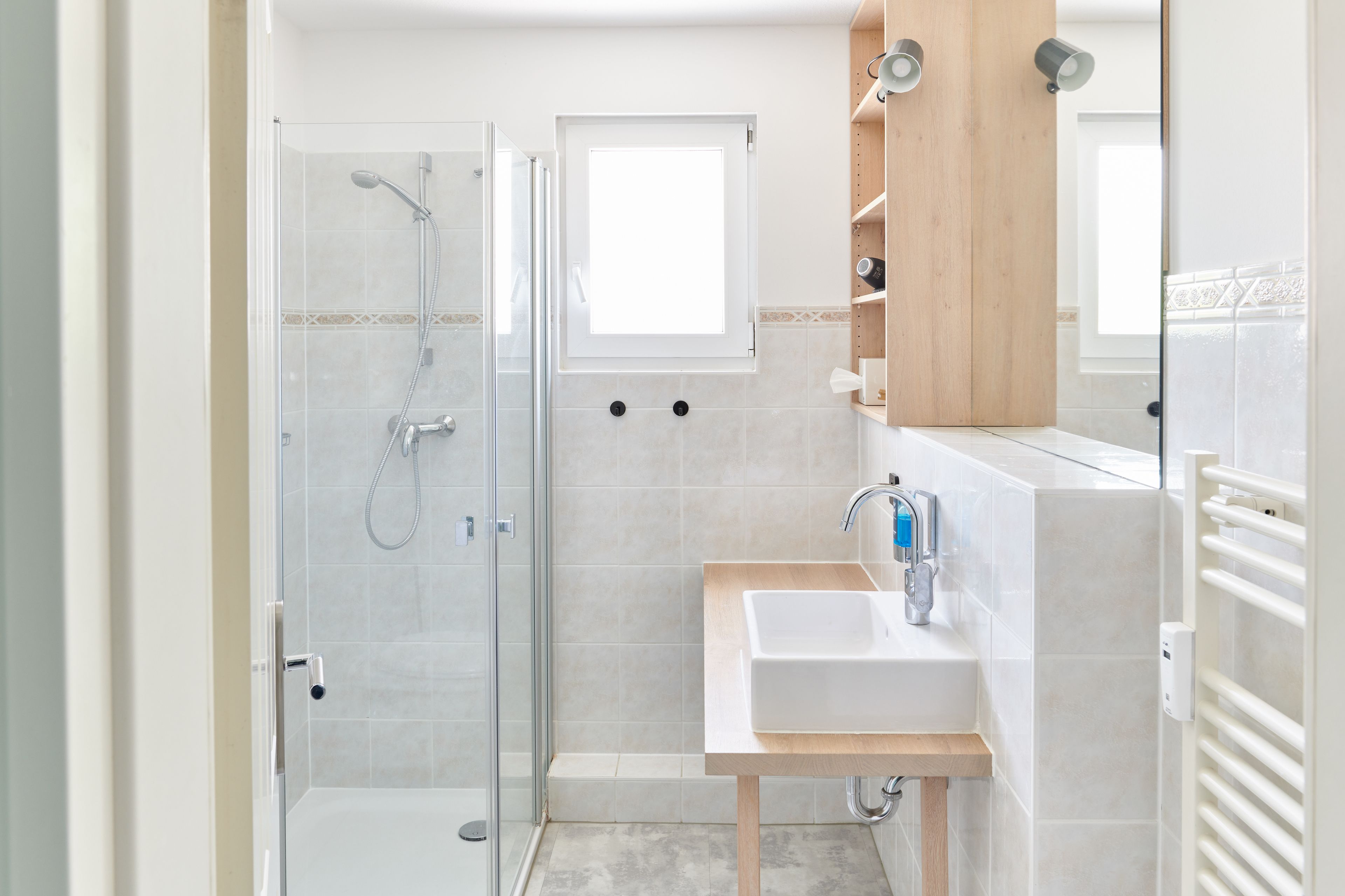 A modern bathroom with a glass shower enclosure, a white sink with a wooden countertop, and a mirror above the sink.