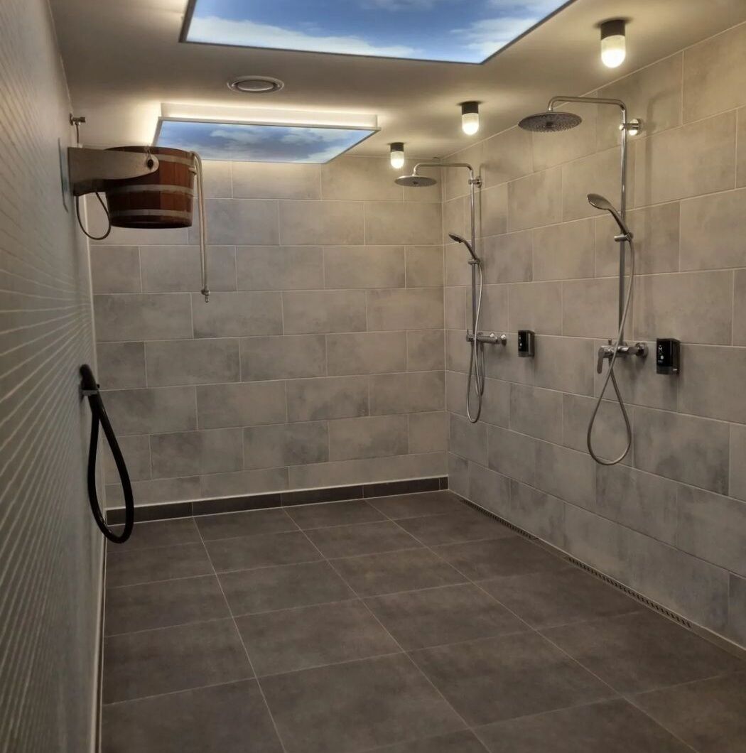 Un baño moderno con azulejos grises, un tragaluz y un cubo de madera.