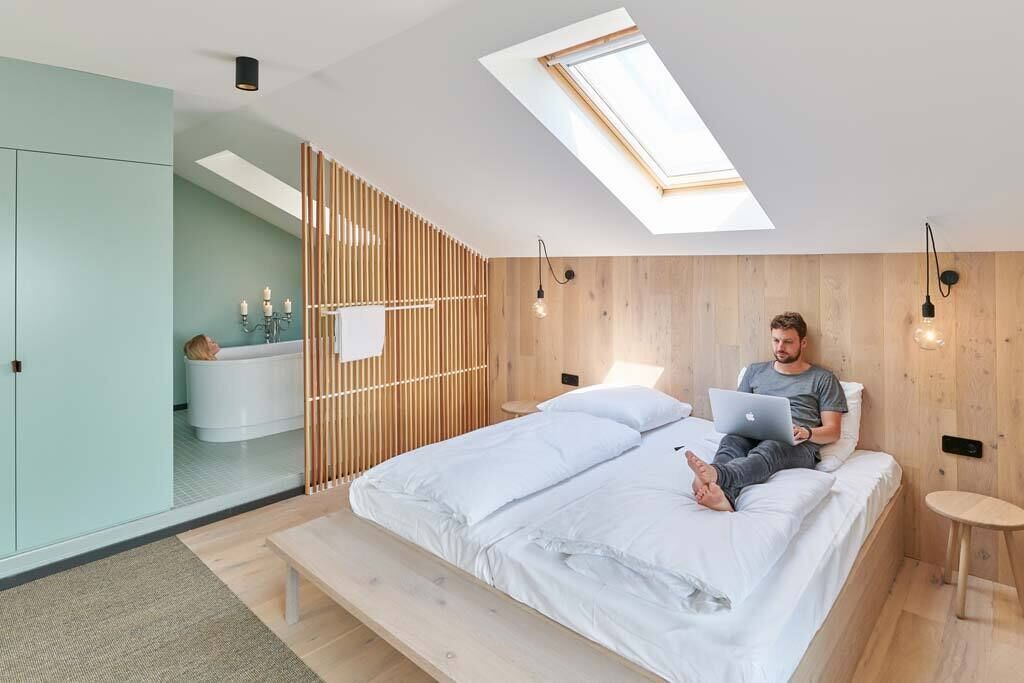 Ein modernes Schlafzimmer mit Oberlicht, einem Bett, einem Laptop und einem kleinen Nachttisch.