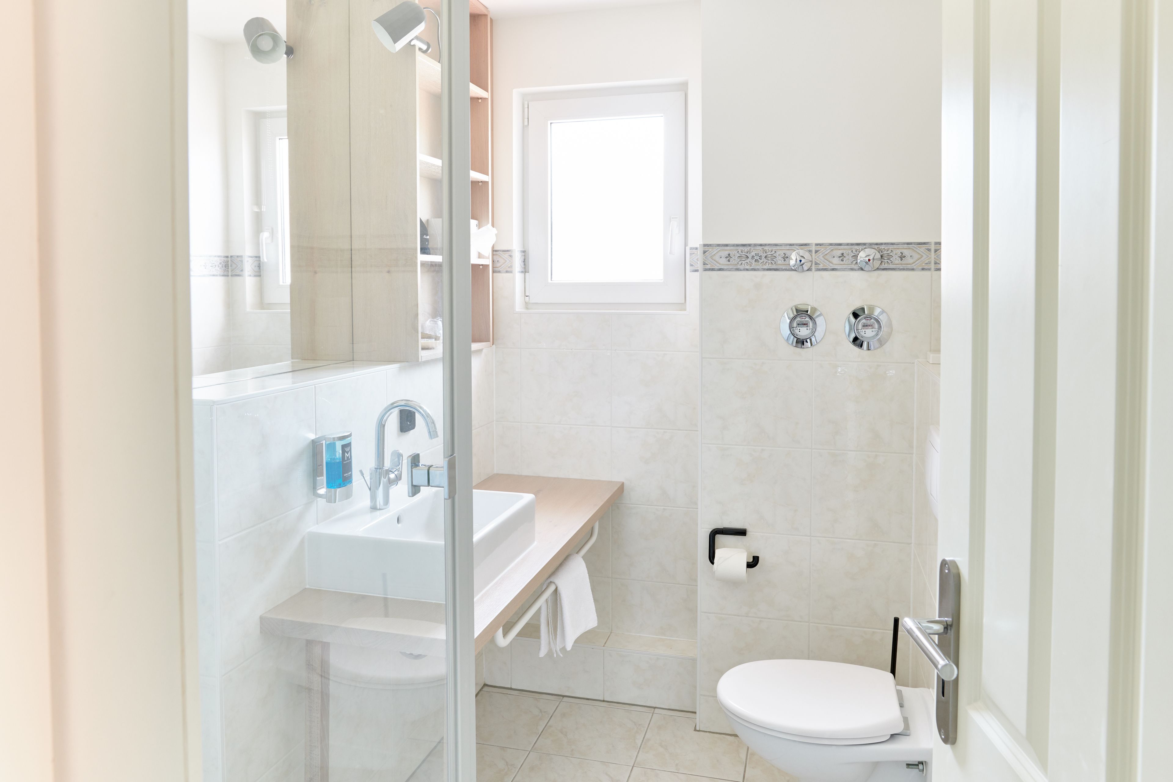 Een moderne badkamer met een douchecabine van glas, een wastafel, toilet en een badkamerkast.