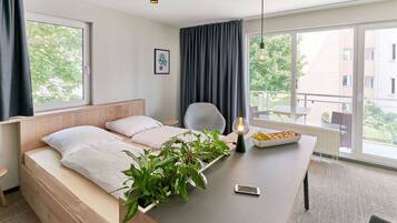 A modern hotel room with a bed, a desk with a lamp, a chair, and a view of the outside.