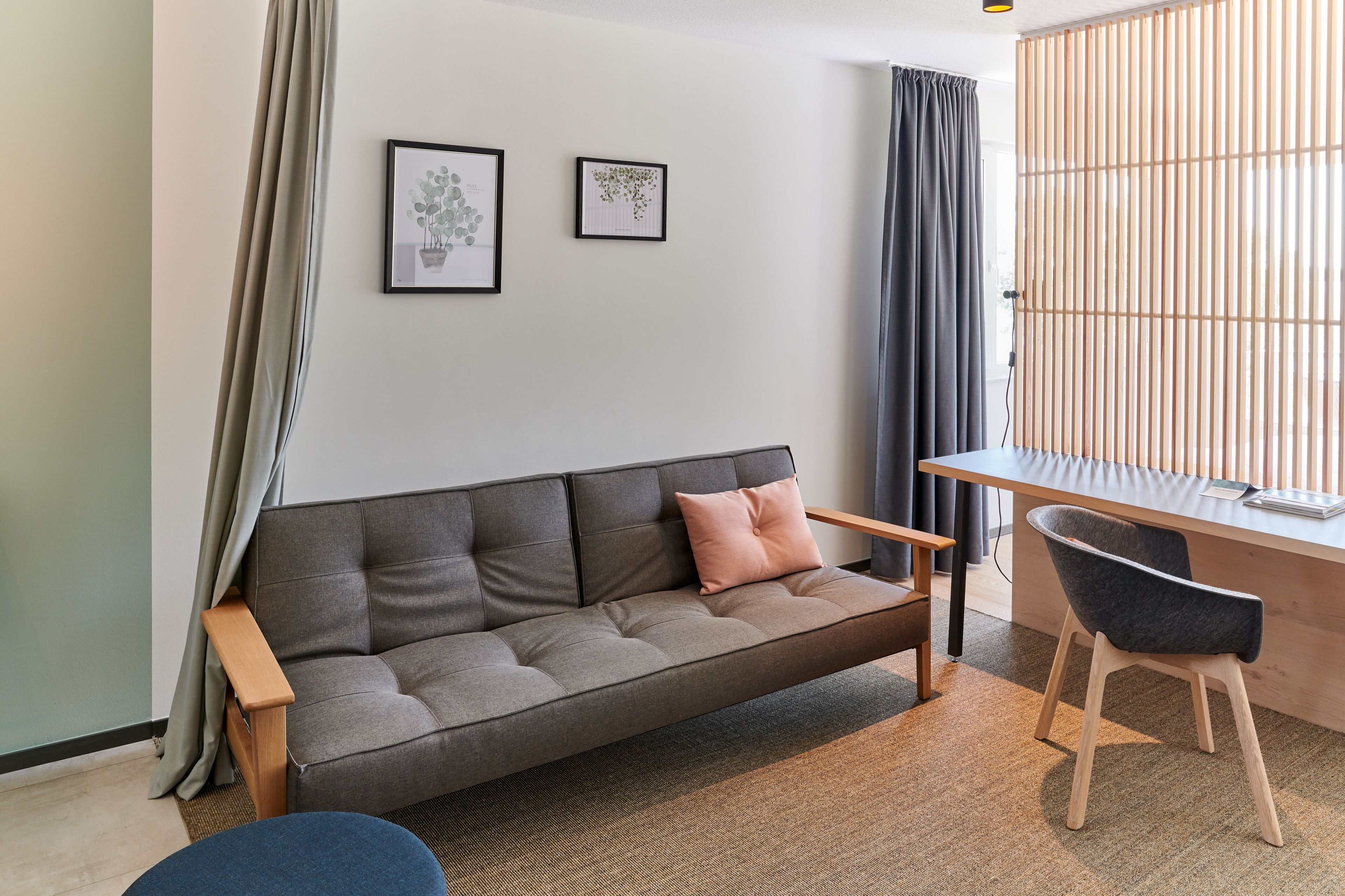 A modern living room with a grey sofa, a wooden desk, and a chair. There are two framed pictures on the wall.