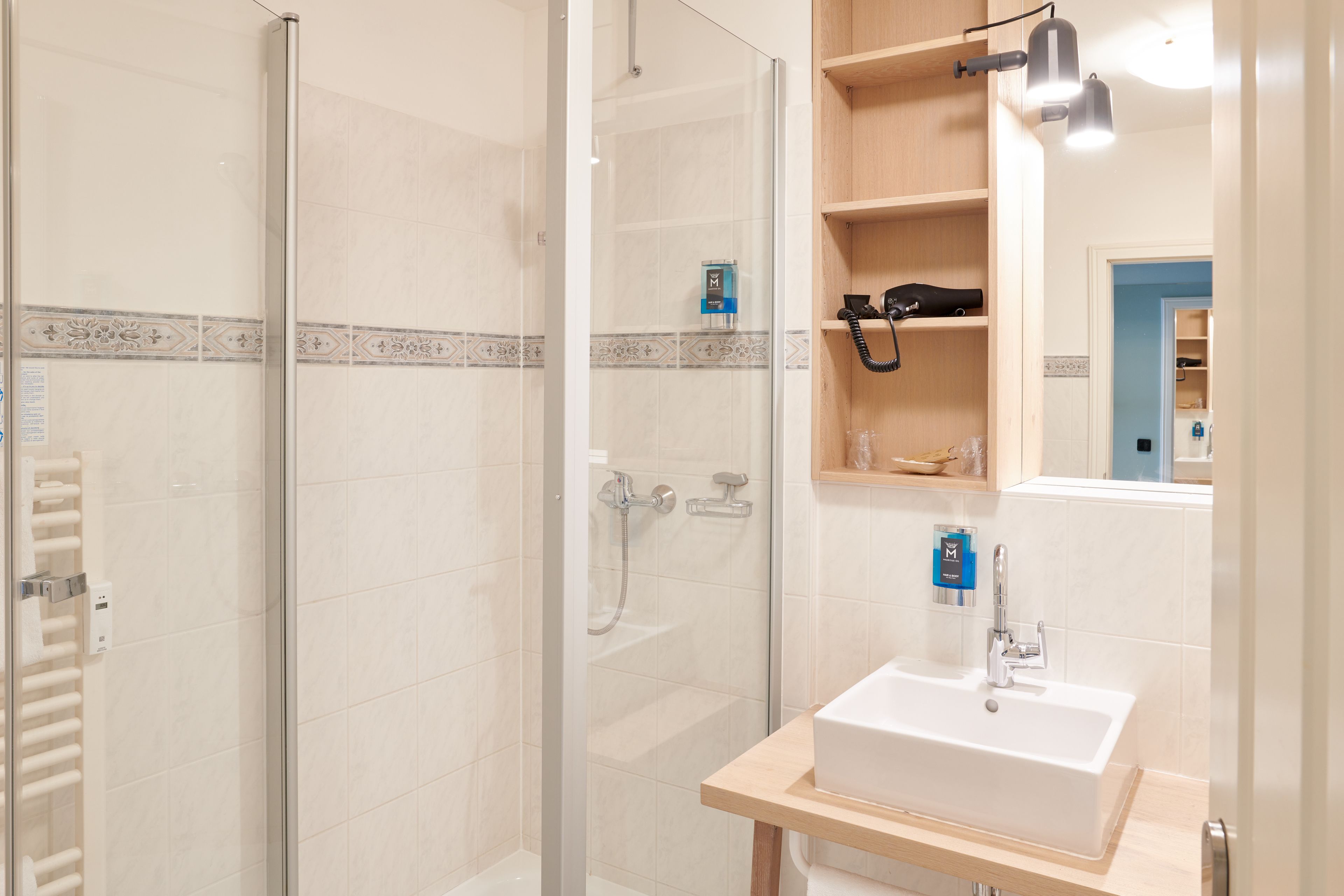 A modern bathroom with a glass shower enclosure, a white sink, and a wooden shelf with toiletries.