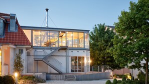 A modern house with a glass facade, a visible staircase, and a well-maintained garden. - Hotel Whitman (Ascheberg)