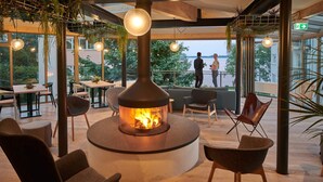 A modern outdoor seating area with a central fire feature, surrounded by chairs and tables, overlooking a body of water. - Hotel Whitman (Ascheberg)
