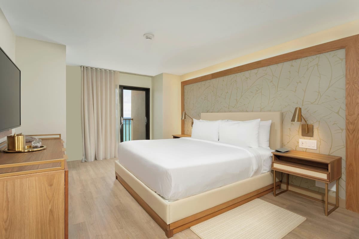 Een hotelkamer met een groot bed, nachtkastje, lamp en een flatscreen televisie.
