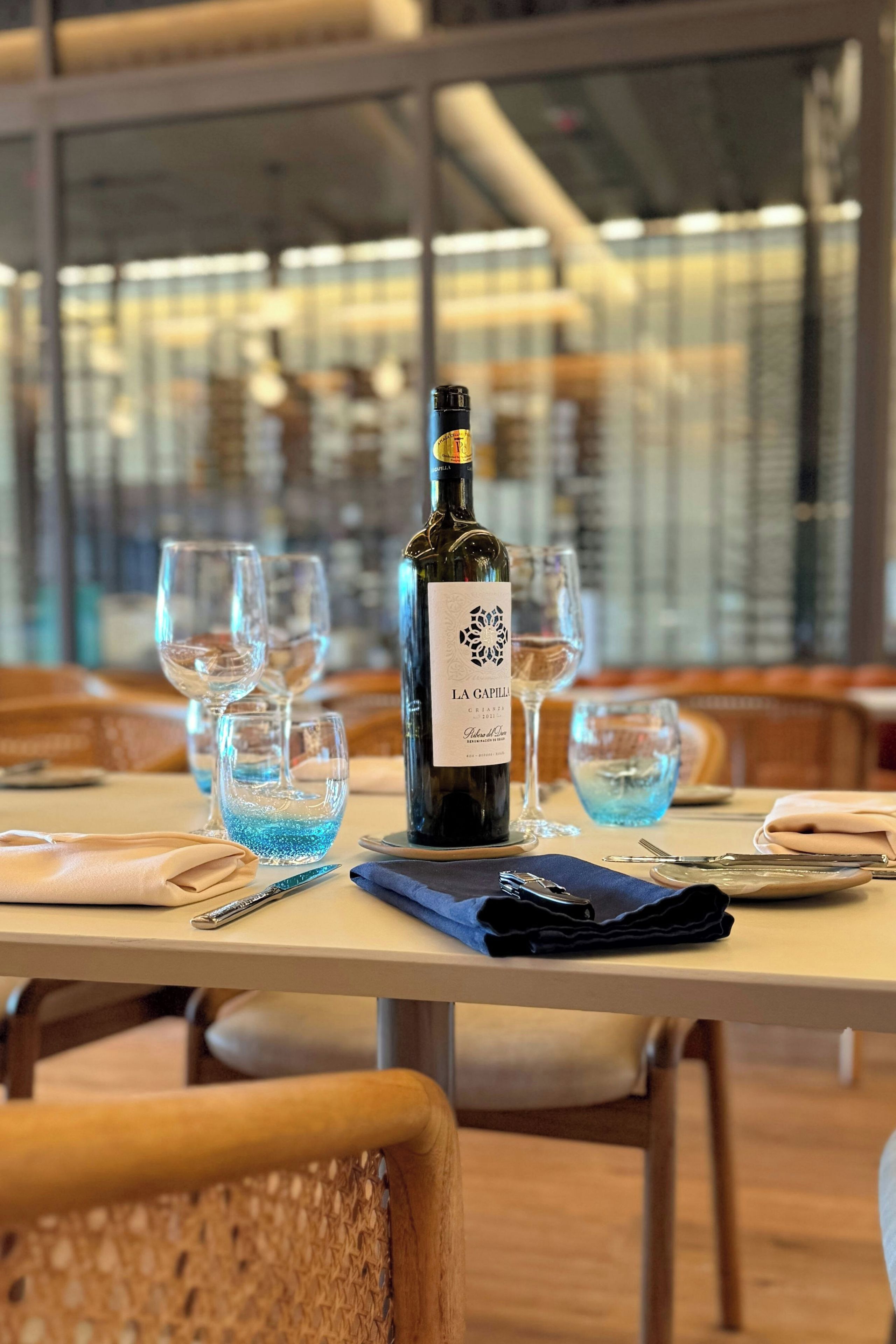A table set with a bottle of wine, glasses, and cutlery in a restaurant with a modern interior.