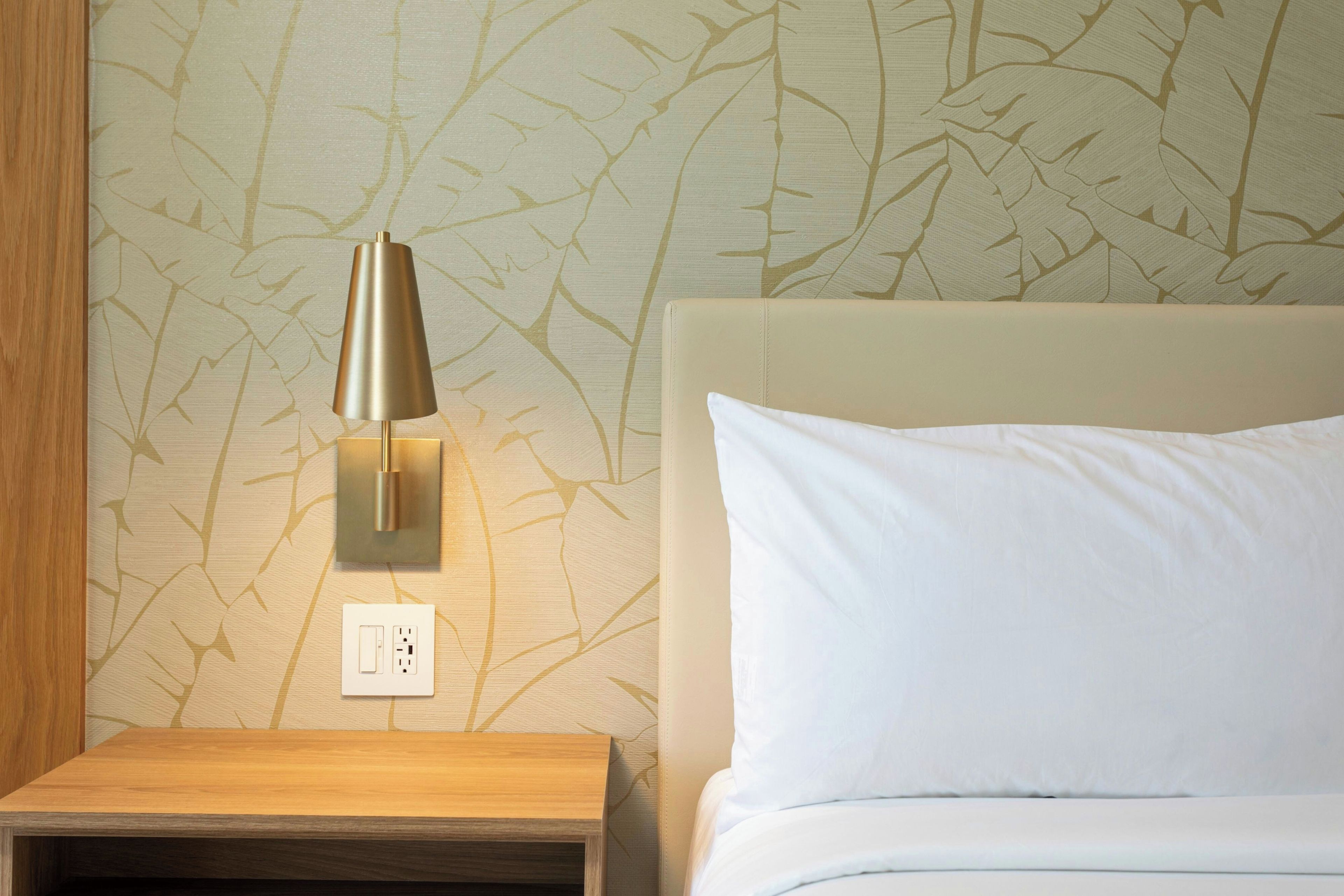 A neatly made bed with a white pillow and a bedside table with a lamp.