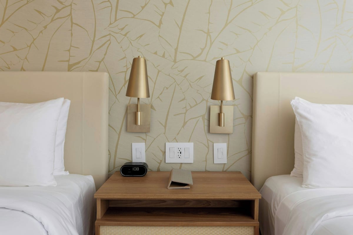 Een hotelkamer met twee bedden, een nachtkastje met een klok en wandlampen.