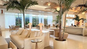 Un amplio vestíbulo de hotel con diseño moderno, que cuenta con una gran zona de estar con sofás y sillones, una recepción y grandes ventanales con vistas al exterior.