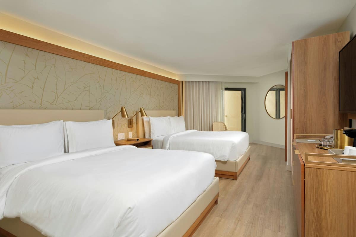 A hotel room with two beds, a wooden headboard, a desk with a mirror, and a view of the hallway.