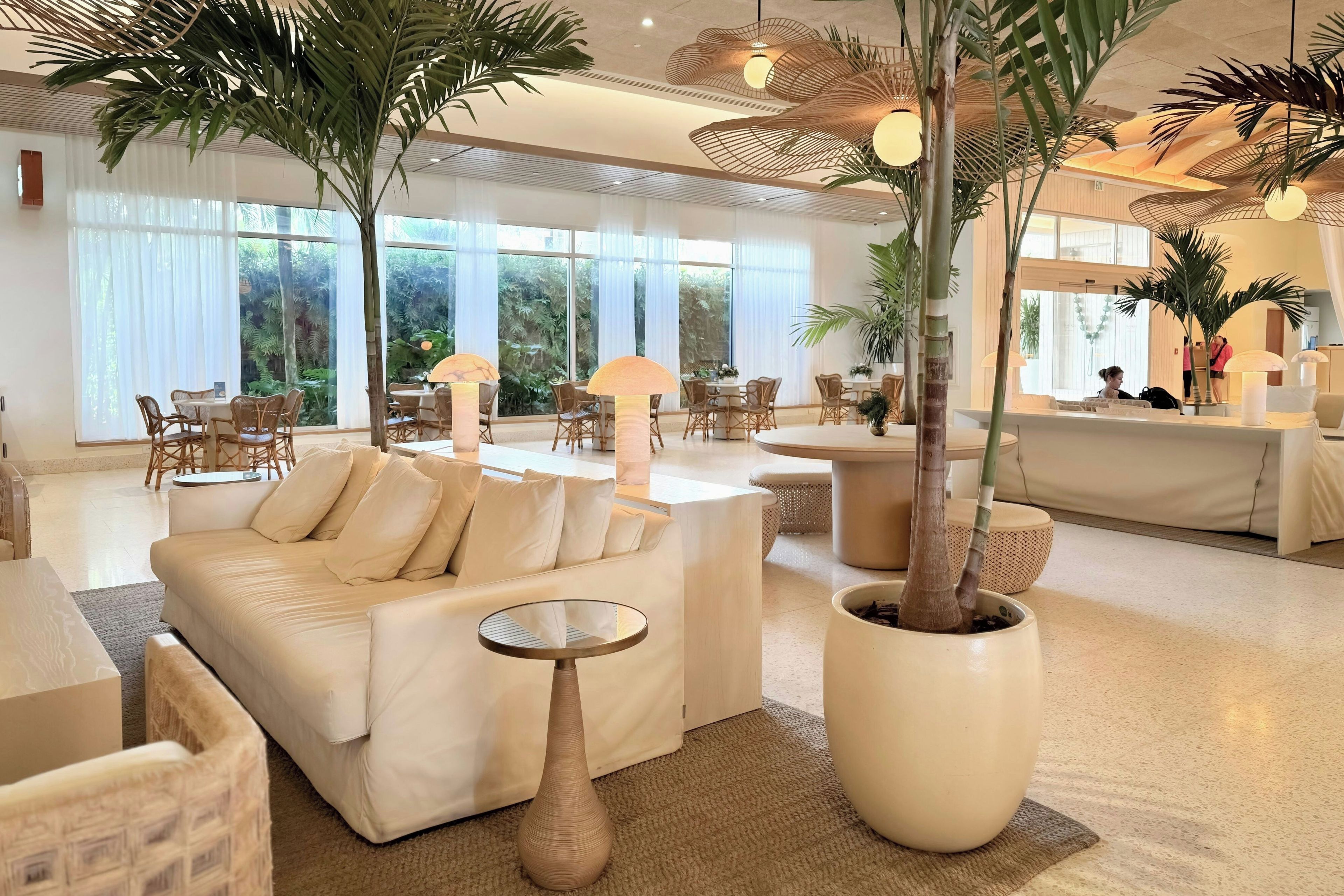 A spacious hotel lobby with a sofa, dining area, and reception desk.