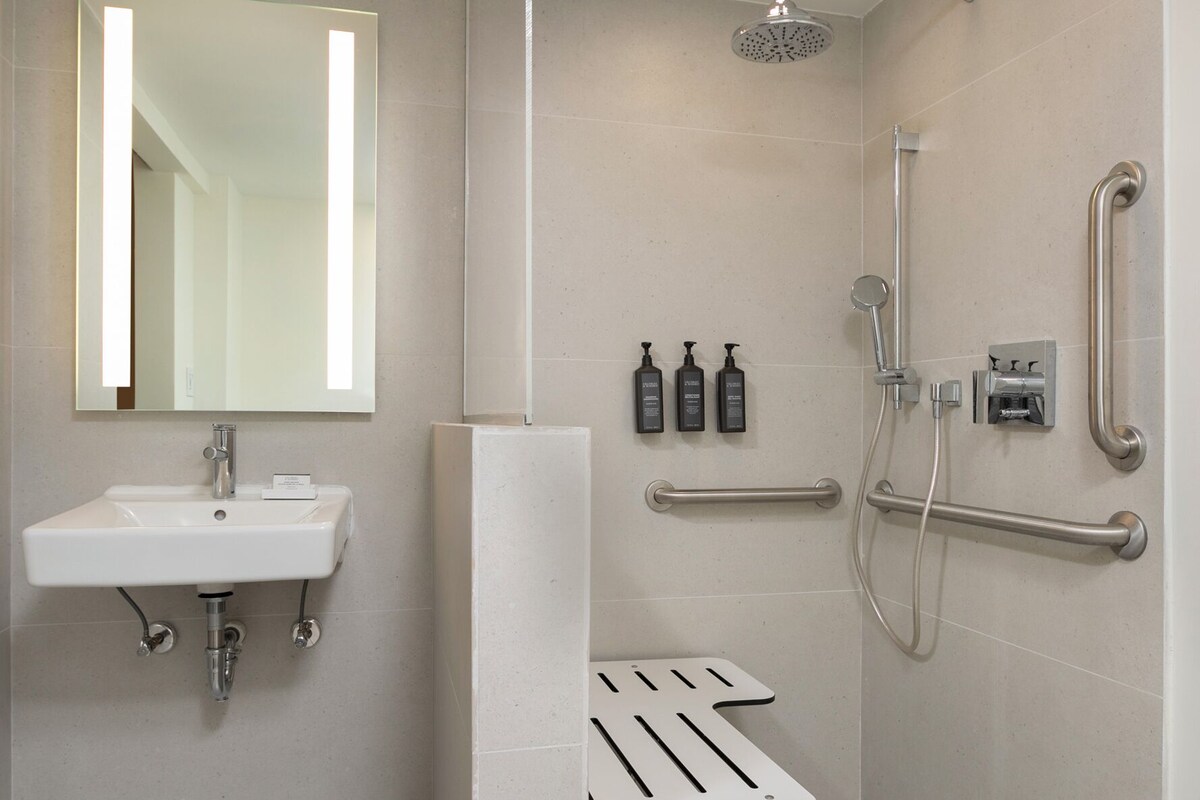 A modern bathroom with a sink, mirror, shower, and grab bars.