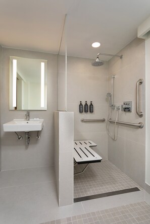 A modern bathroom with a sink, mirror, shower, and grab bars.