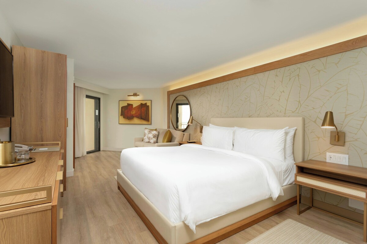 A hotel room with a large bed, bedside tables, a desk with a lamp, and a painting on the wall.