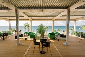 A covered outdoor seating area with tables and chairs, overlooking the ocean.