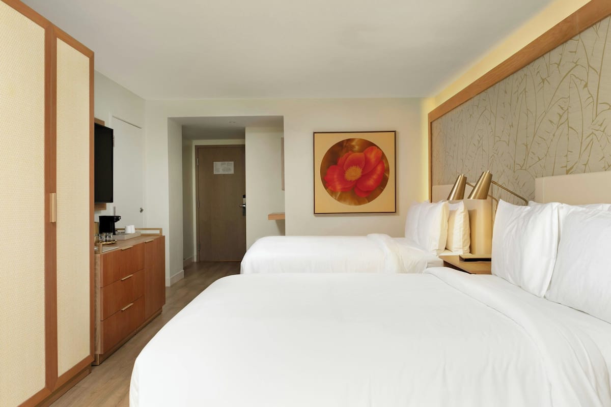 Een hotelkamer met twee bedden, een houten garderobe, een koffiezetapparaat en een groot bloemschilderij aan de muur.