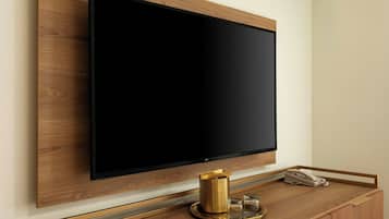 A flat-screen TV mounted on a wooden wall, a brass coffee pot, and a telephone on a wooden counter.