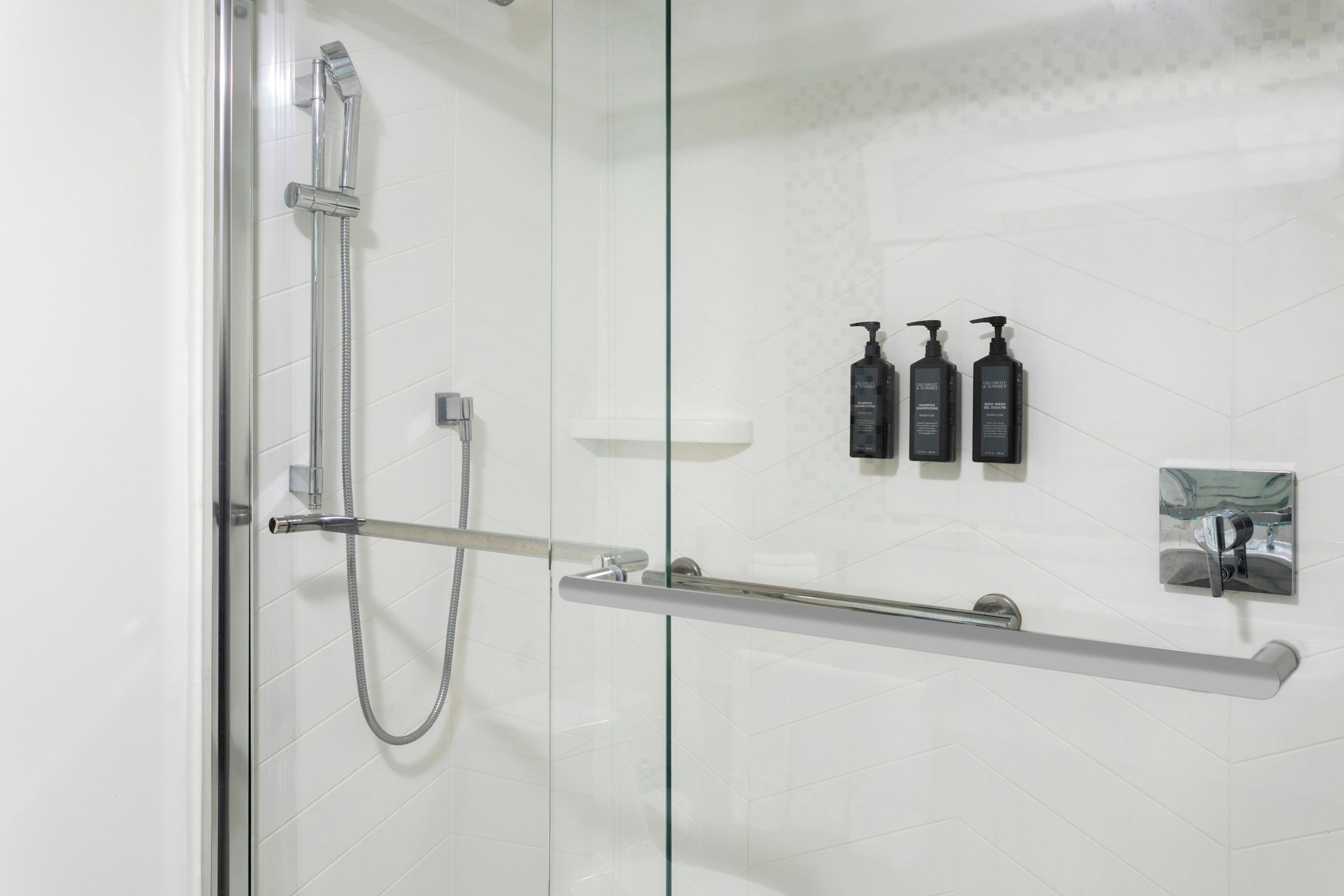 A modern bathroom with a glass shower enclosure, a handheld showerhead, a glass shelf with toiletries, and a towel rack.