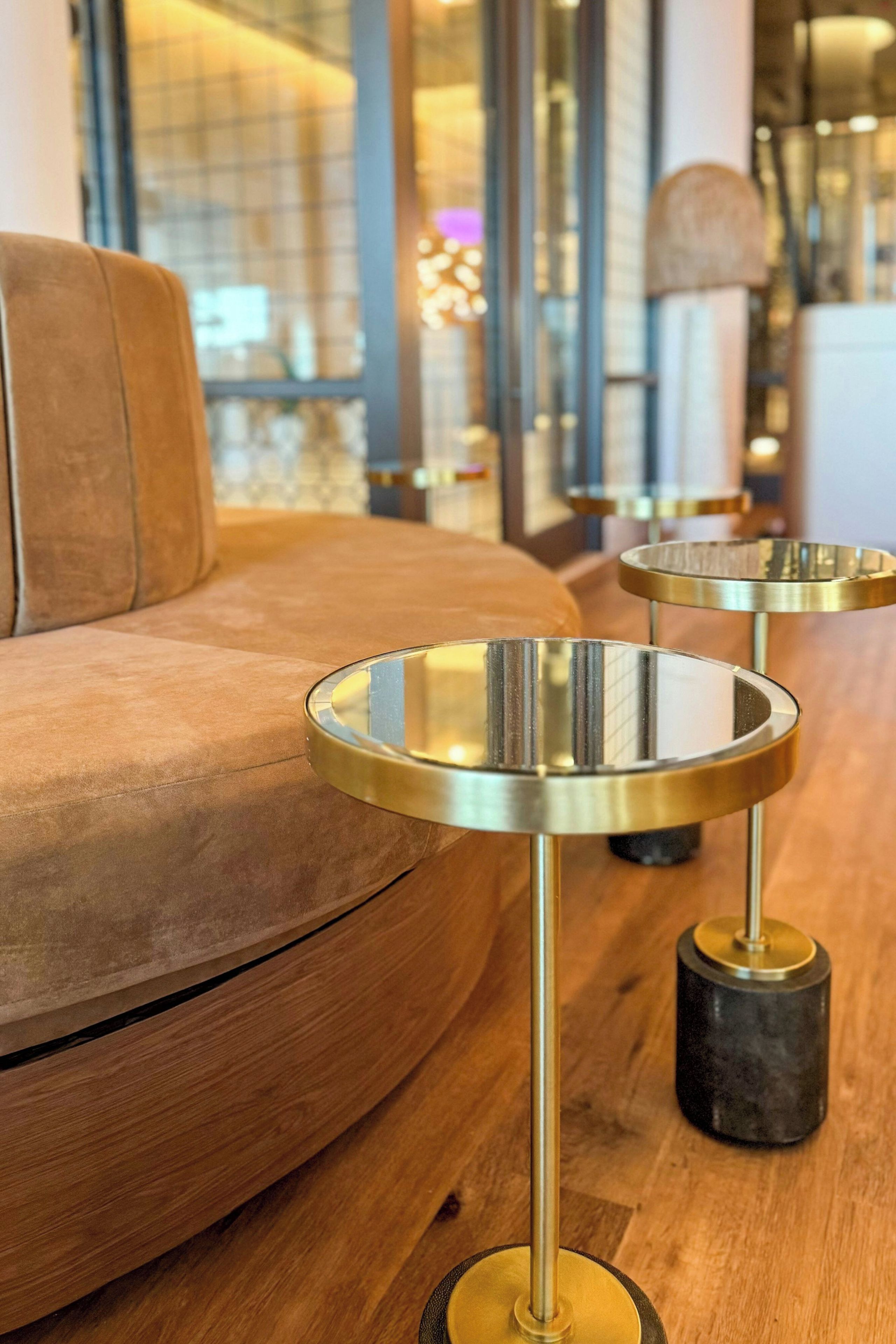 A modern interior with a leather sofa and two metallic round tables with black bases.