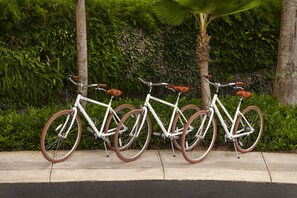 Trois vélos sont garés contre un mur, avec de la verdure en arrière-plan.