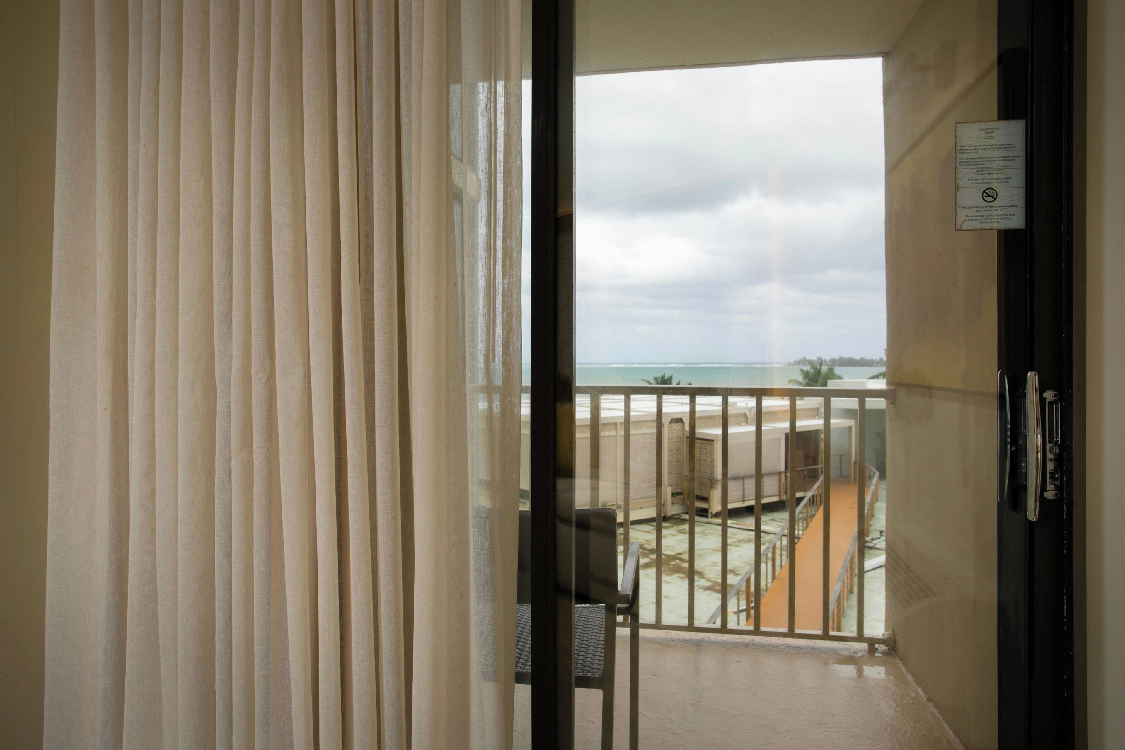 Un balcon avec vue sur l’océan, une porte avec une pancarte et une chaise.