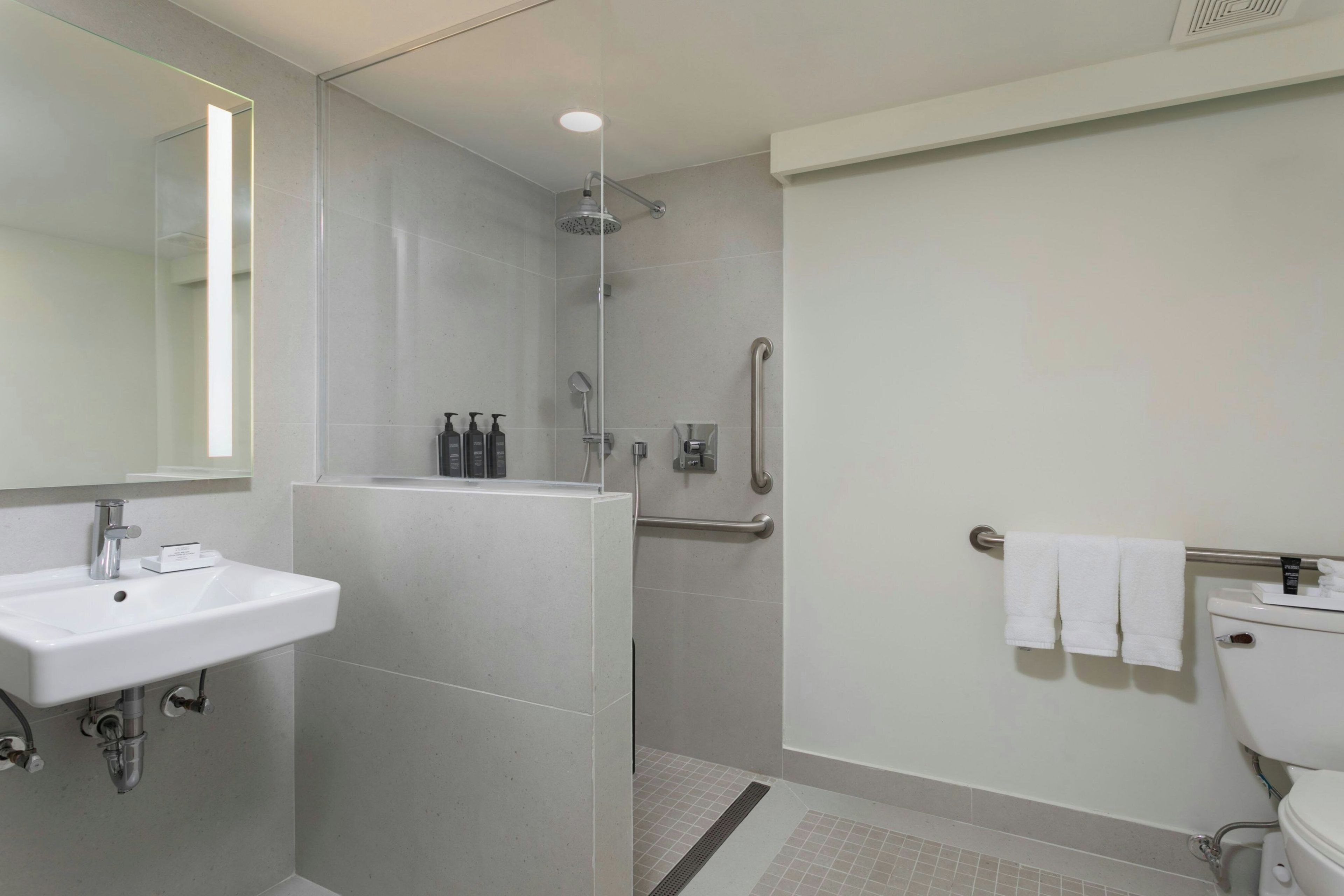 Un baño moderno con lavamanos, espejo, ducha e inodoro.