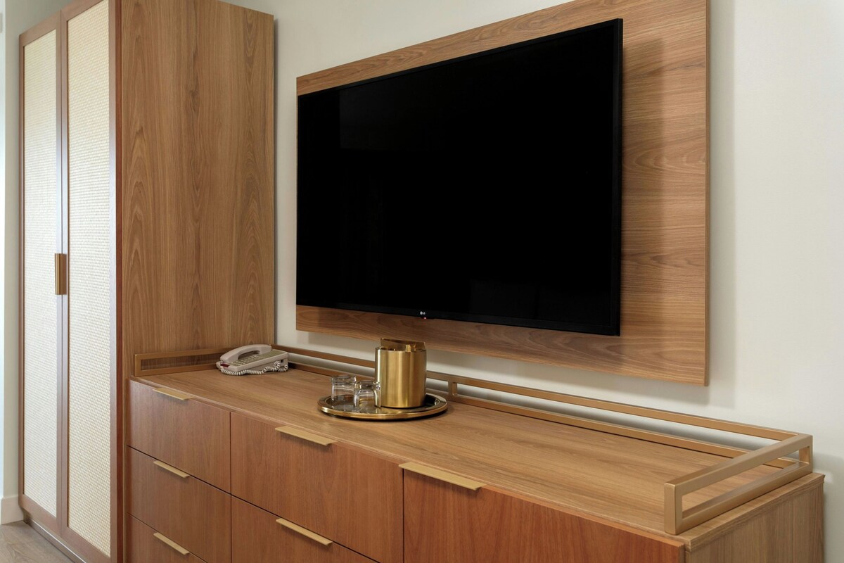 A wooden cabinet with a flat-screen TV mounted above it, a telephone, and a small decorative item on the counter.