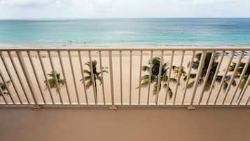 A beach view with a railing, palm trees, and a clear sky.