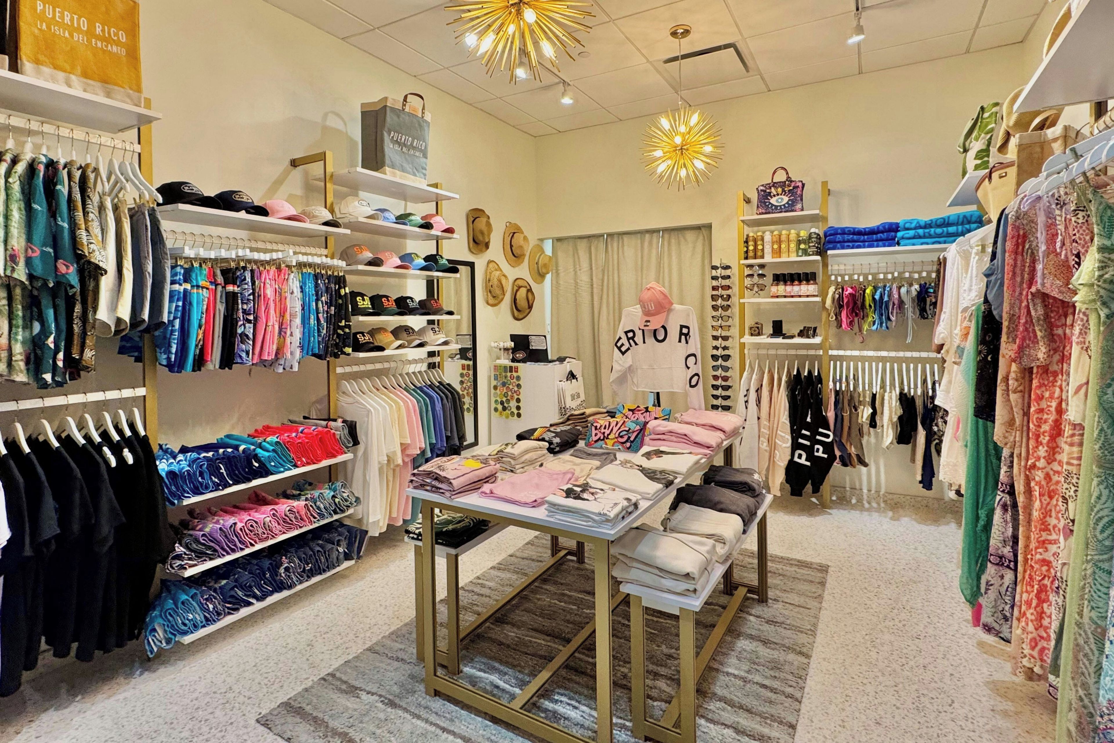 A retail store with clothing racks, a display table, and various hats.