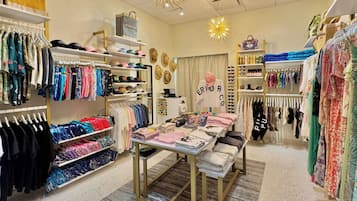 A retail store with clothing racks, a display table, and various hats.