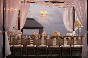 An outdoor wedding venue with string lights, a chandelier, and floral centerpieces on tables.