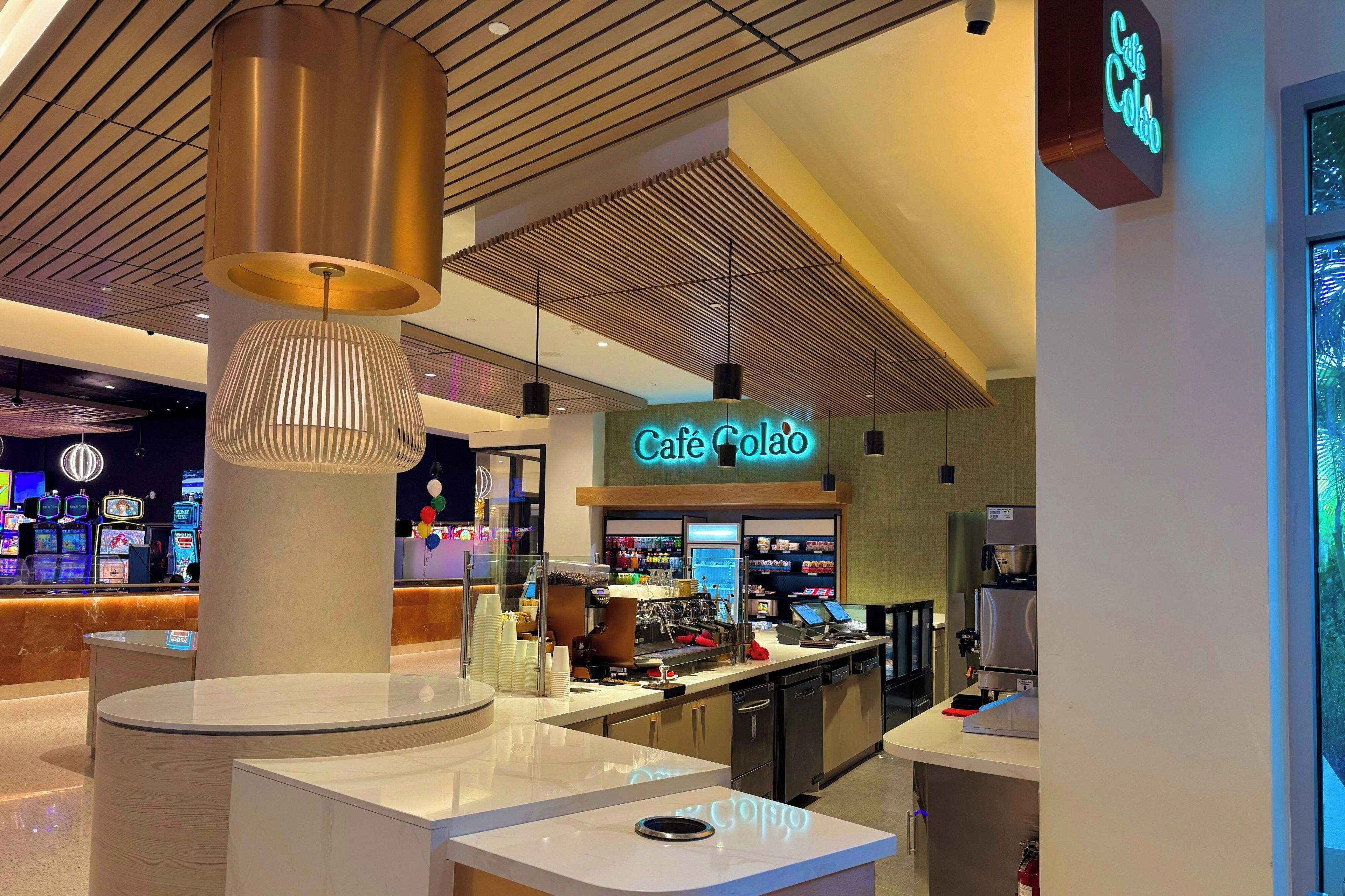 A modern café interior with a central counter, a neon sign, and a ceiling with a wooden slat design.