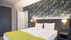 A hotel room with a bed, a nightstand, a wall-mounted lamp, and a door. - Thon Residence Parnasse (Brussels)