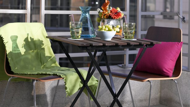 A table with a glass pitcher, a bowl of fruit, and two glasses on a balcony with a view of a modern building. - Thon Residence Parnasse (Brussels)